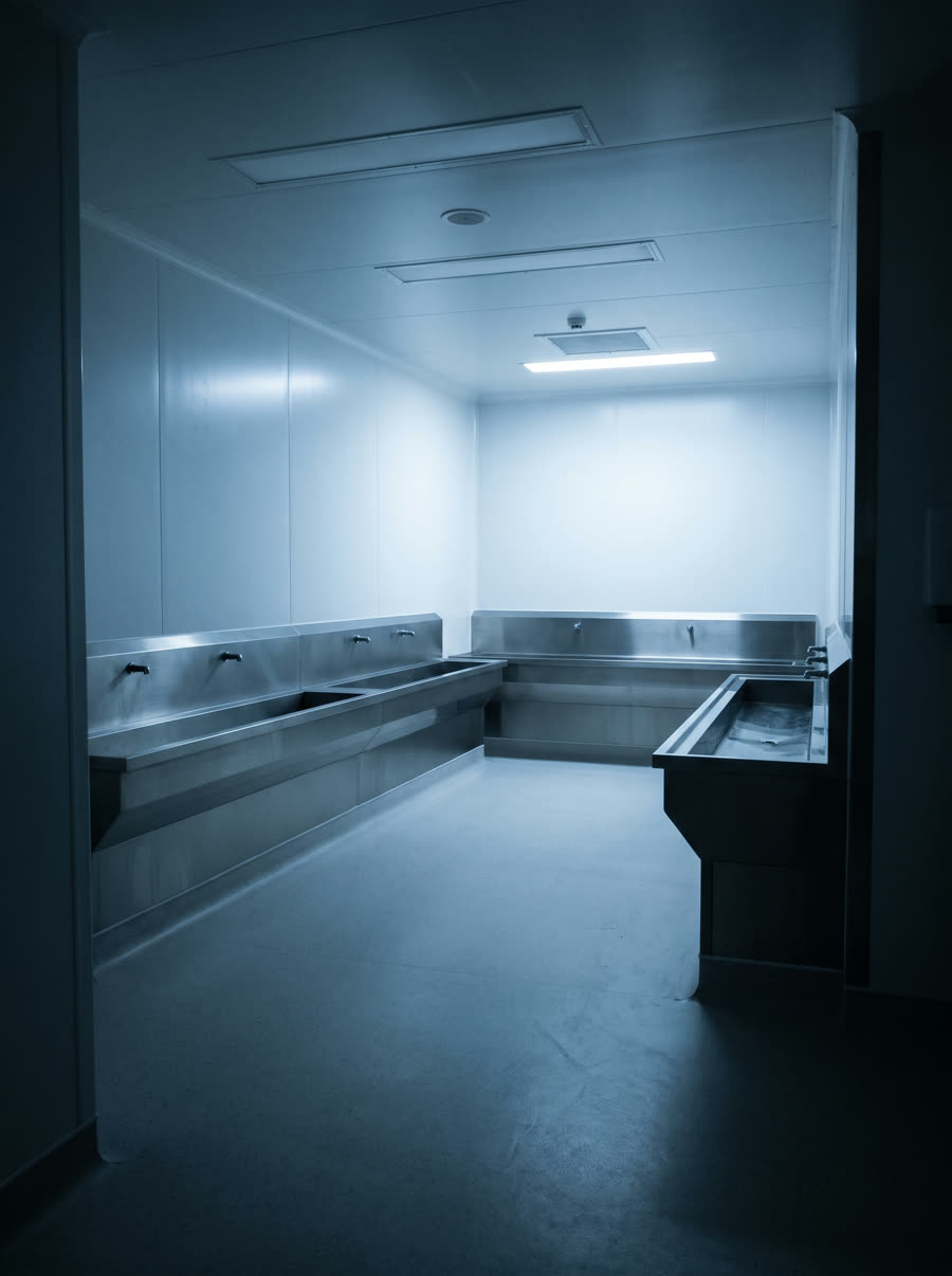 An empty sterile processing room with stainless benching against clad walls.